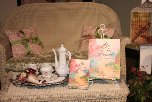 Go in Peace book by Cherie Fresonke, set on a white wicker chair next to a tea set